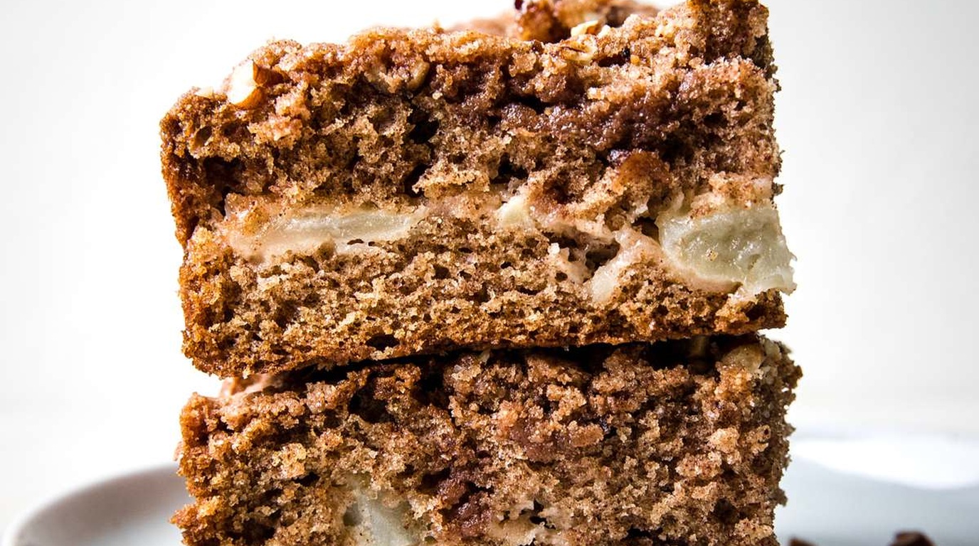 Ultra close-up macro cross-section of moist cinnamon apple crumb cake showing tender baked apple chunks, spiced cake crumb, and thick brown sugar pecan streusel