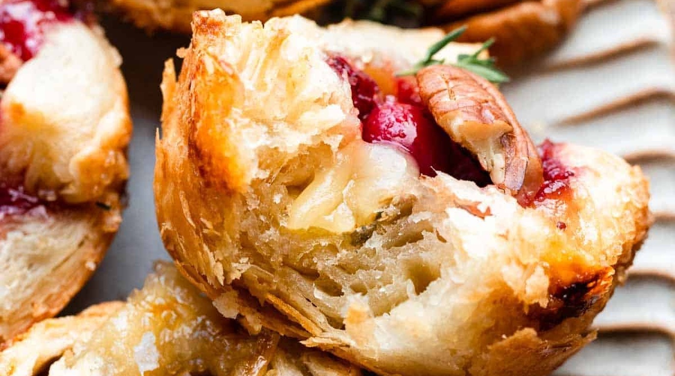 Ultra close-up macro of flaky golden baked puff pastry cranberry brie bites with melted gooey cheese and ruby cranberry sauce