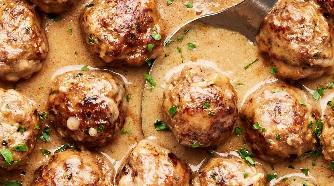 Ultra close-up macro of tender beef meatballs bubbling in a rich creamy garlic parmesan sauce in a cast iron skillet