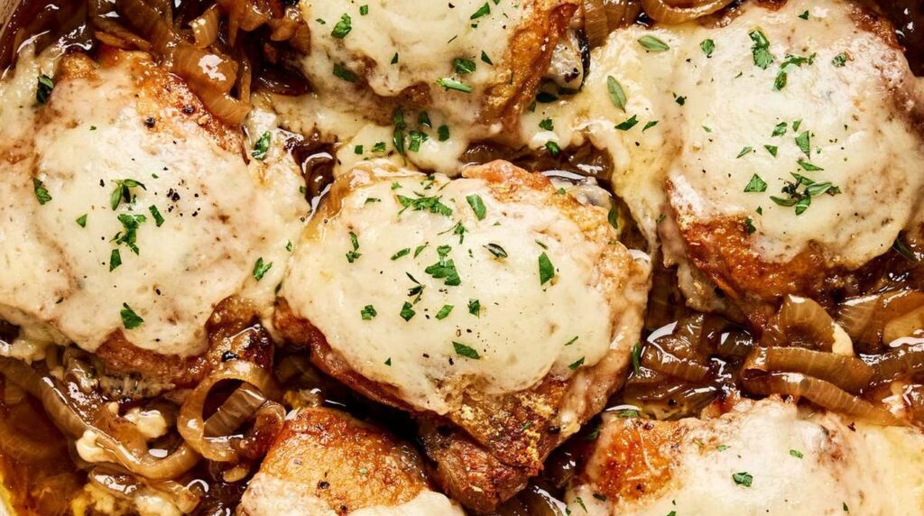Ultra close-up macro of French onion chicken skillet with golden crispy chicken thighs smothered in caramelized onions and bubbling melted Gruyère cheese