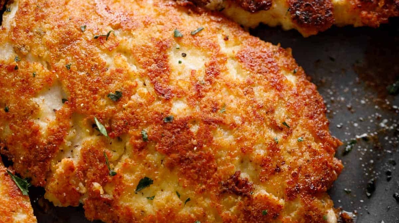 Ultra close-up macro food photography of crispy golden garlic parmesan crusted chicken with fresh herbs and lemon