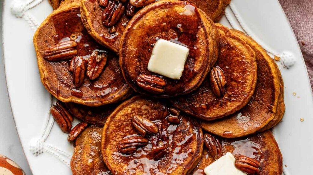 Ultra close-up macro of a tall golden stack of fluffy pumpkin buttermilk pancakes with melting spiced maple butter and pure amber maple syrup