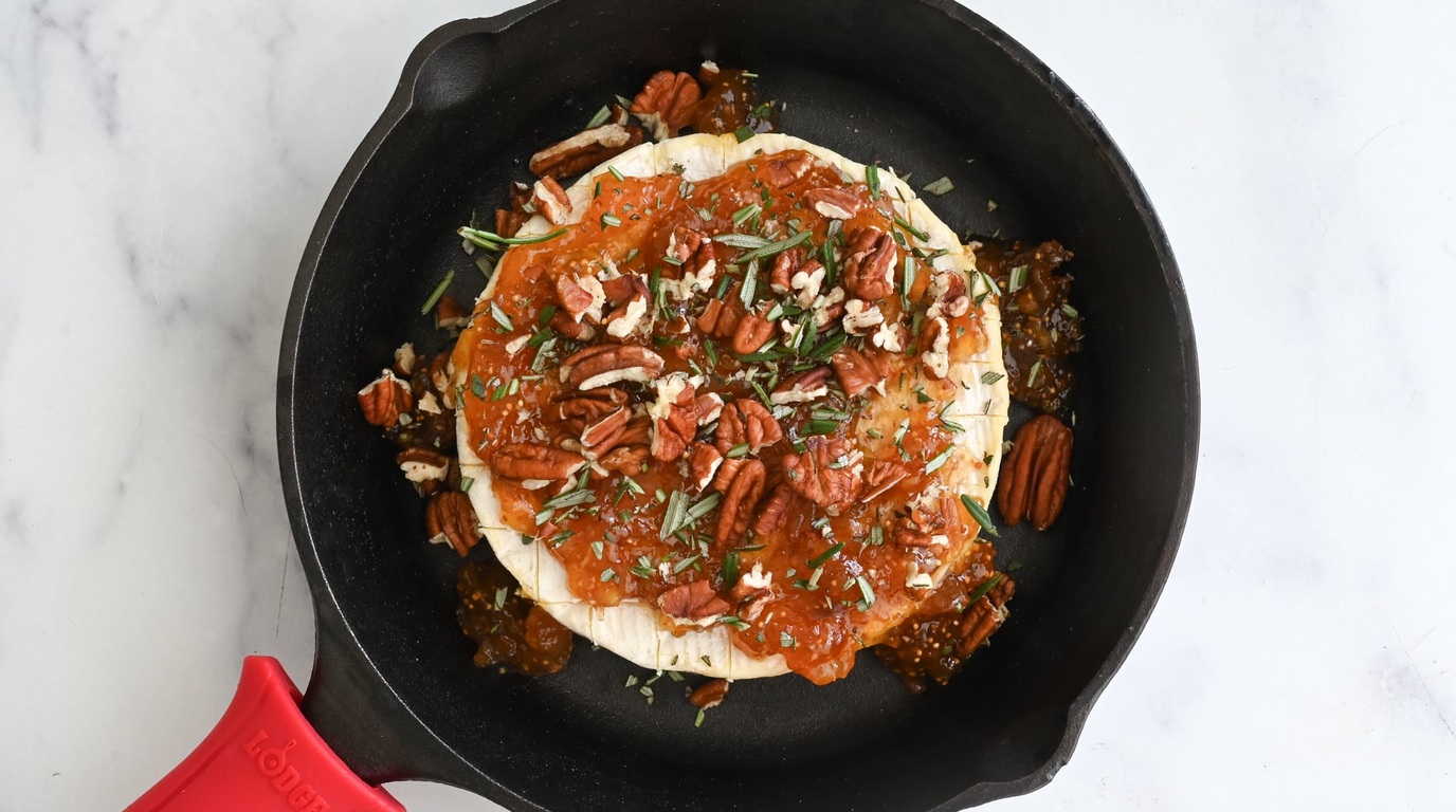 Ultra close-up macro of bubbling gooey melted brie in skillet topped with toasted pecans honey and fresh rosemary