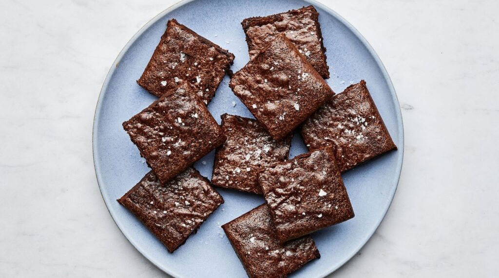 Ultra close-up macro of dense, fudgy chocolate brownies showing shiny crinkly papery top crust and melted dark chocolate pockets