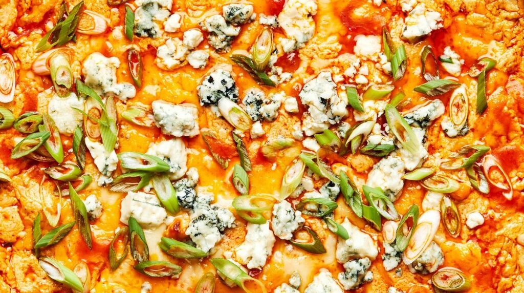 Ultra close-up macro of bubbling golden baked buffalo chicken dip with melted cheddar and mozzarella cheese in a cast-iron skillet