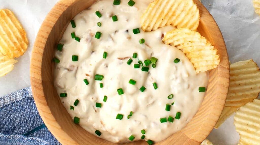 Ultra close-up macro of creamy caramelized French onion dip in a wooden bowl with ridged potato chips