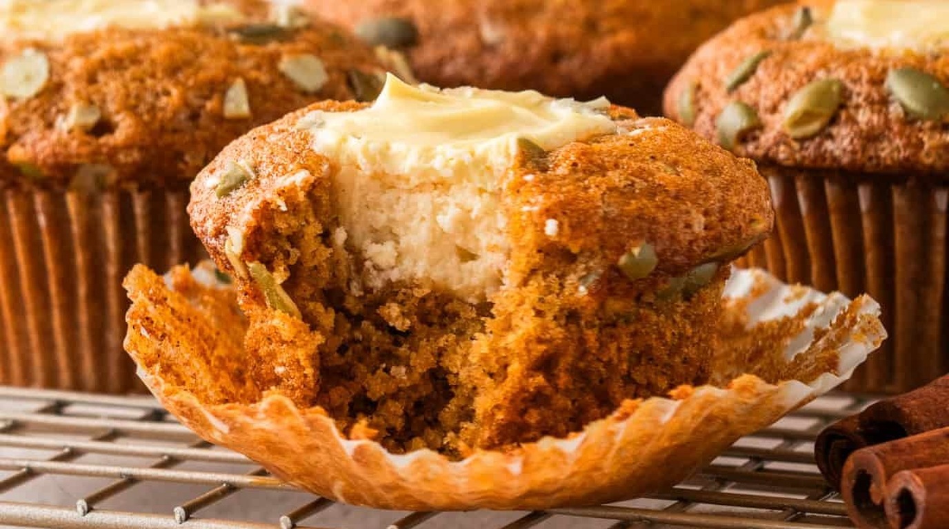 Ultra close-up macro of golden baked pumpkin cream cheese muffins with sweet cream cheese swirl and roasted pepitas