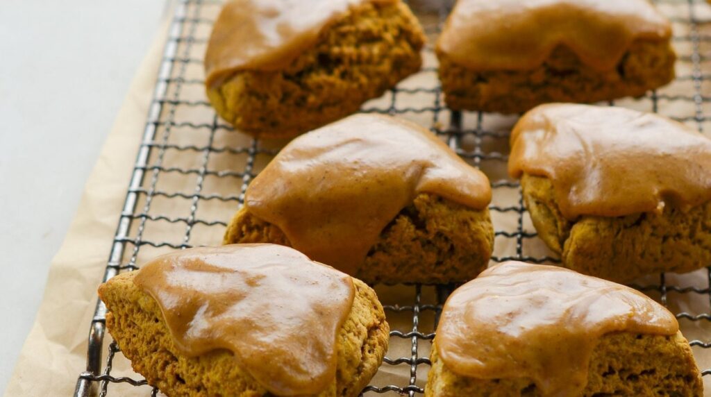 Ultra close-up macro of tender glazed pumpkin scones with spiced drizzle on wire rack
