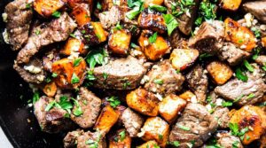 Ultra close-up macro of sizzling garlic butter steak bites and caramelized sweet potatoes in a cast-iron skillet