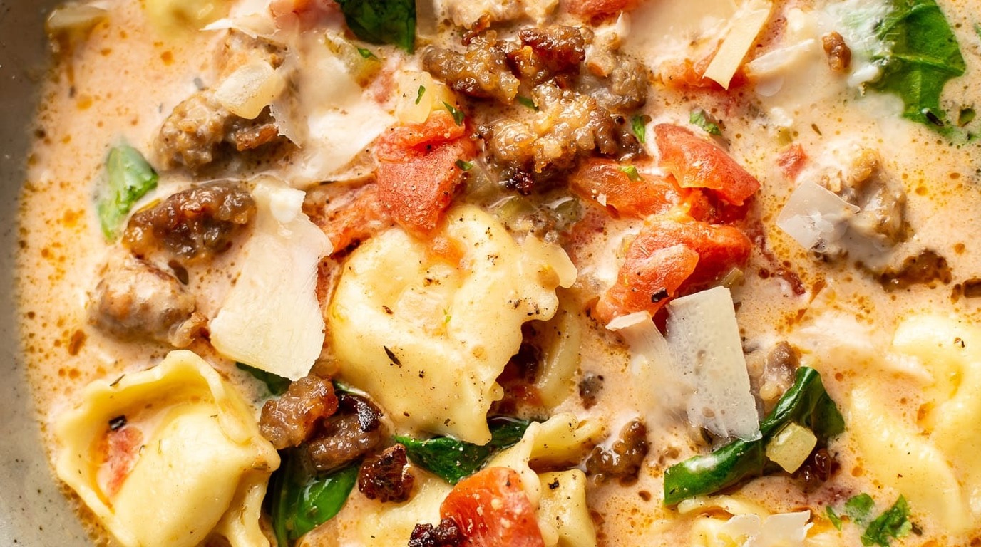 Ultra close-up macro of creamy italian sausage tortellini soup with plump cheese tortellini, savory sausage, and wilted spinach in rich tomato cream broth