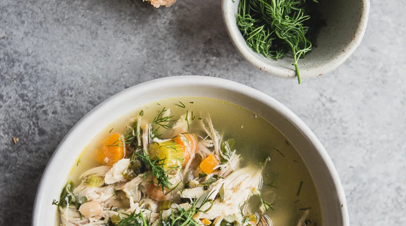 Ultra close-up macro of vibrant lemon herb white bean chicken soup with tender shredded chicken, cannellini beans, and fresh dill in a ceramic bowl